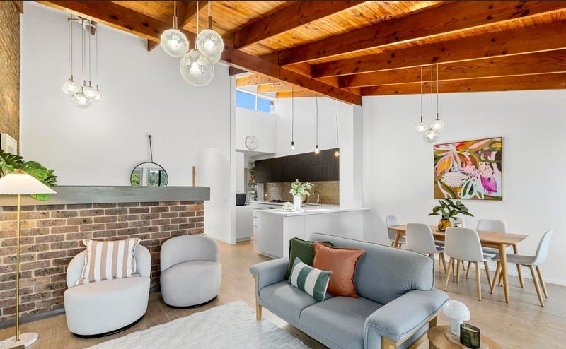 Living room with an exposed brick fireplace feature and open kitchen beyond