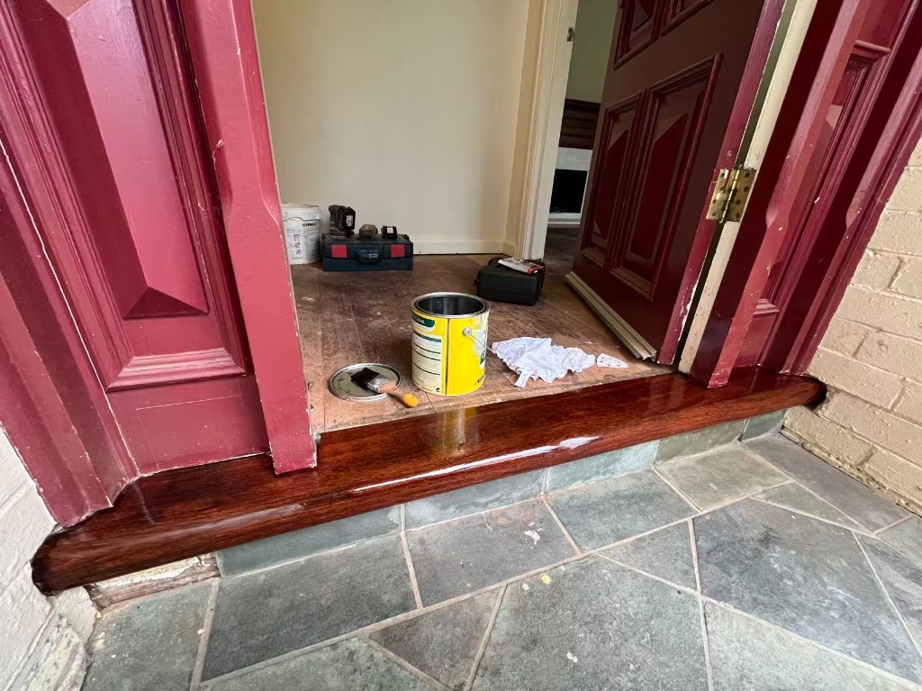 Restained front door timber sill with burgundy door and entry during internal works
