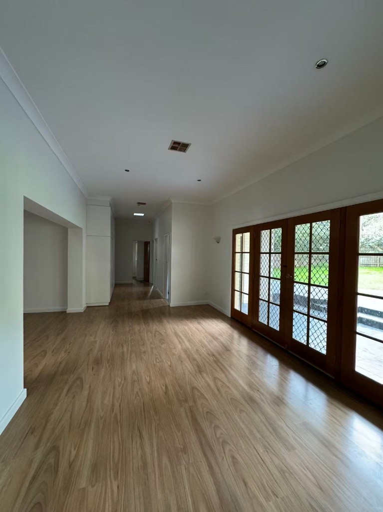 Bright unfurnished living area with French doors and hallway beyond after repaint