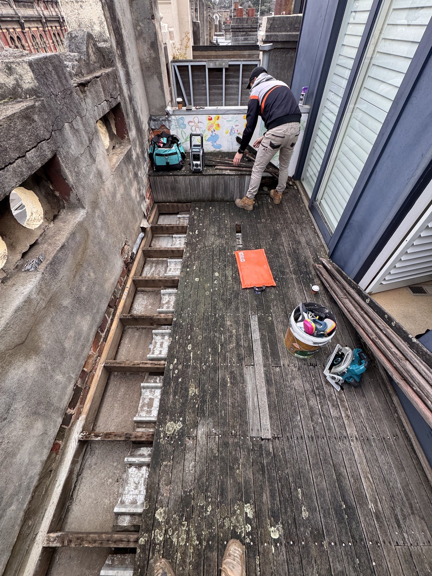 Old weathered merbau rooftop deck being lifted, exposing the joists beneath