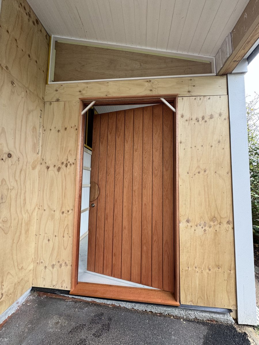 Completed front door installed in the plywood-clad porch